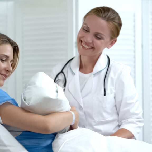 Happy mother holding newborn baby, smiling doctor looking at child, motherhood