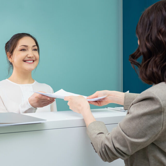 receptionist accepts documents from the female visitor.