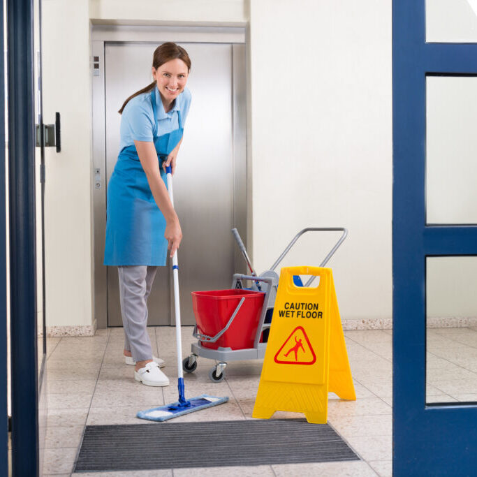 Happy Female Worker In Uniform Cleaning Floor With Mop